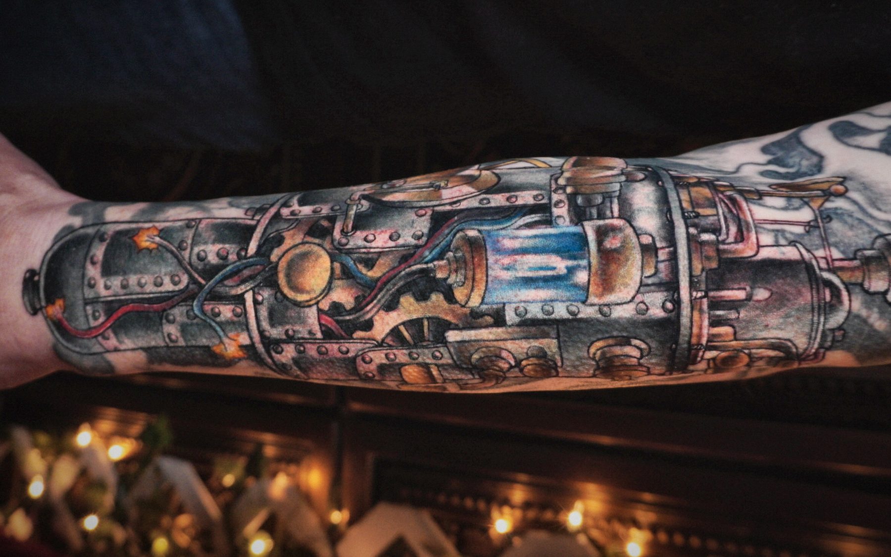 A detailed biomechanical tattoo of riveted steel machinery — pistons, gears, valves and copper piping — covering a forearm.
